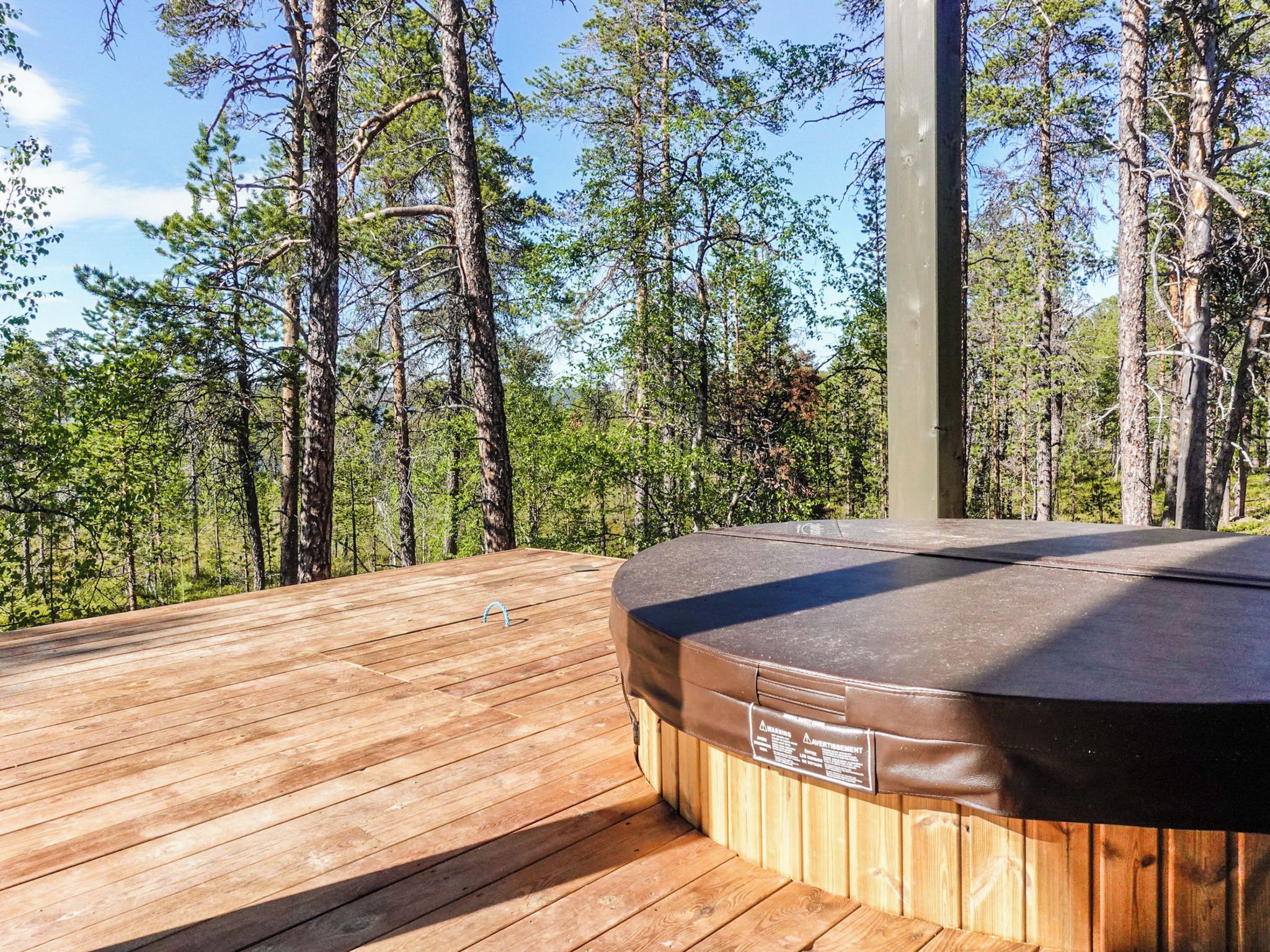 A wooden deck with a hot tub, surrounded by a forest.
