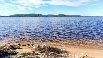 Une plage à l’eau claire, bordée de galets, avec des collines qui se dessinent à l’horizon.