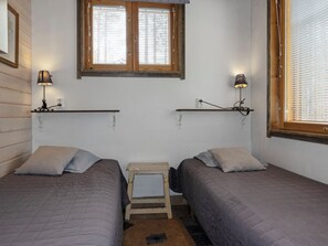 Une chambre avec deux lits, une petite table et une fenêtre avec des stores.