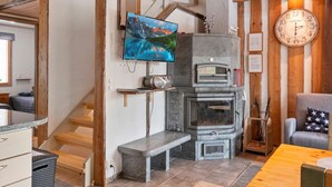 A cozy living area with a stone fireplace, a television mounted on the wall, and a wooden staircase.