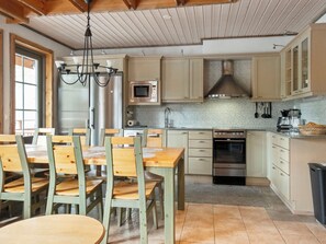 A kitchen with wooden cabinets, a stainless steel refrigerator, a microwave, a stove, and a dining area with wooden chairs and a table.