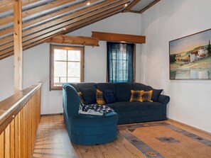 Une pièce chaleureuse avec un plafond en bois, un canapé, un fauteuil et un tableau accroché au mur.