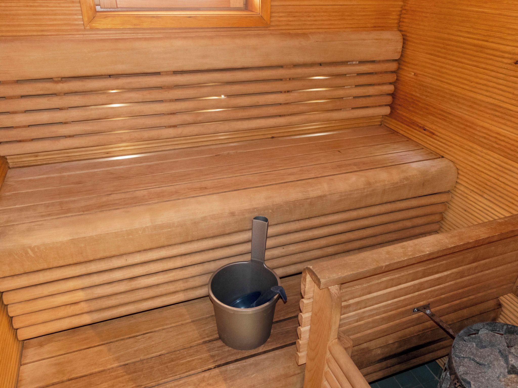 A sauna with wooden benches and a metal bucket.