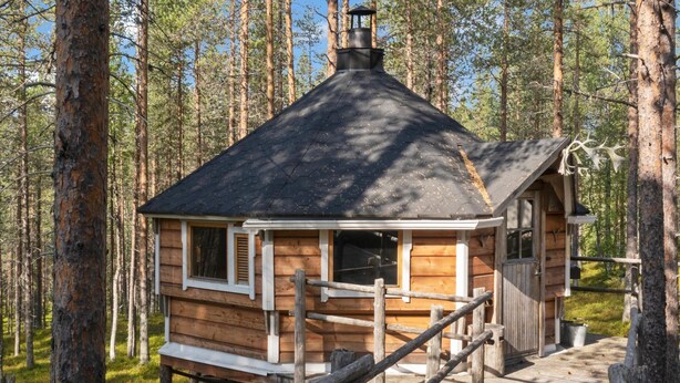 A wooden cabin with a steeply pitched roof, a chimney, and a wooden deck leading to the entrance.
