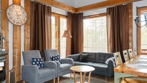 A cozy living room with a wooden ceiling, a large clock, and a dining area with a wooden table and chairs.