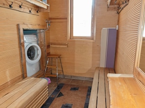 Een kleine houten kamer met een wasmachine, een kruk en een bank.
