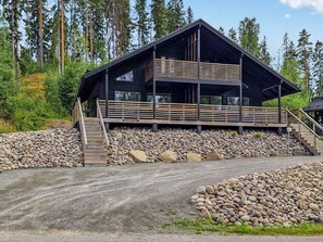 Un chalet à deux étages doté d’une terrasse en bois et de fondations en pierre.