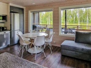 Une cuisine moderne équipée d’appareils électroménagers en acier inoxydable, un coin repas avec une table ronde et des chaises, et une vue sur une zone boisée grâce à de grandes fenêtres.