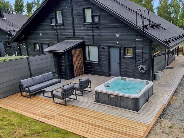 A modern outdoor deck with a hot tub, seating area, and a wooden deck.