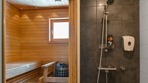 Una sauna con una panca di legno, una finestra, una zona doccia con dispenser di sapone e un cestino.