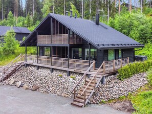 Una cabaña moderna con cimientos de piedra, terraza de madera y una escalera empinada que conduce a la entrada.