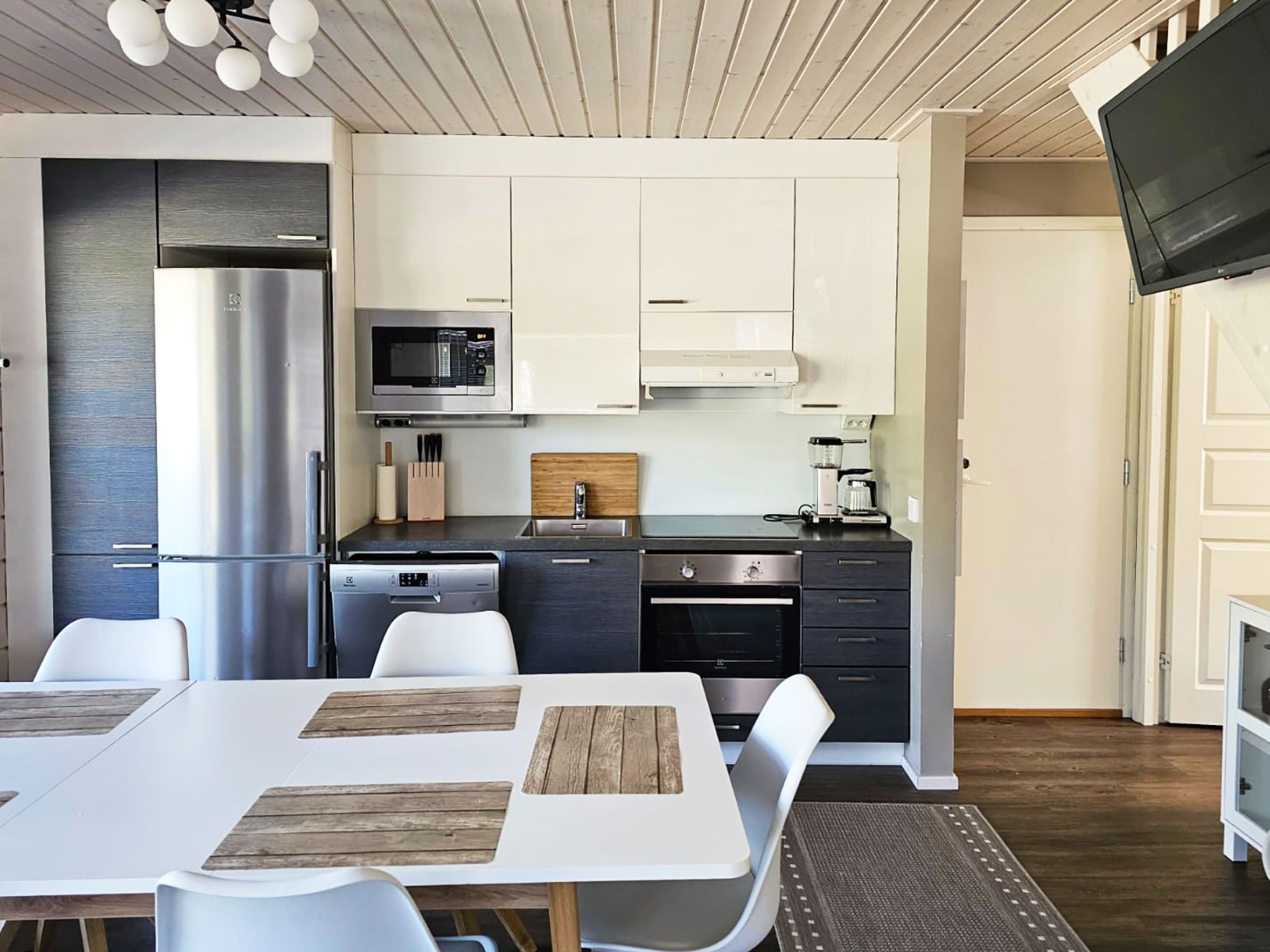 Una cucina moderna con mobili bianchi, elettrodomestici in acciaio inossidabile e una zona pranzo con sedie bianche e un tavolo in legno.