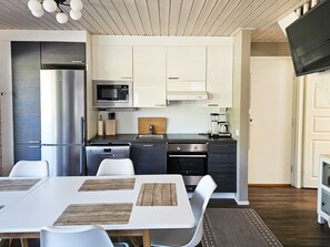 Une cuisine moderne avec des meubles blancs, des appareils en acier inoxydable et un coin repas comprenant des chaises blanches et une table en bois.