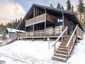 A multi-level wooden cabin with a balcony, wooden stairs, and a snow-covered ground. - Himoksen keiju 1 by Interhome (Kuhmoinen)