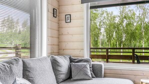 Un sofá seccional gris con almohadones, una pared de madera y vistas a árboles a través de una ventana.