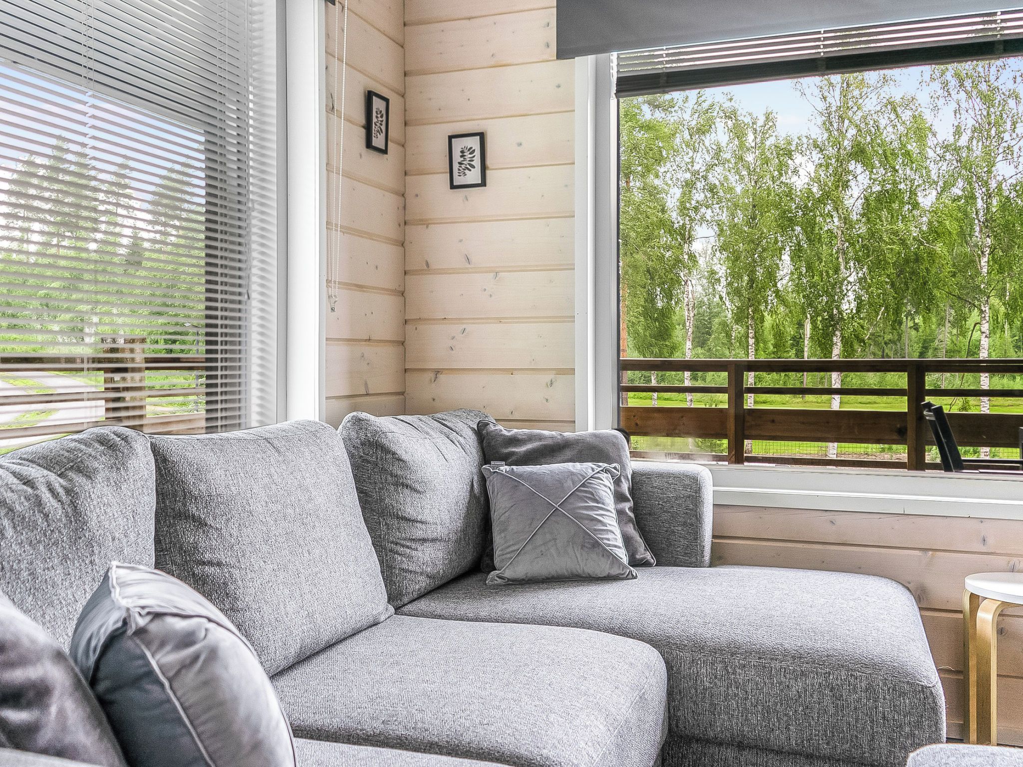 A grey sectional sofa with cushions, a wooden deck, and a view of trees through a window.