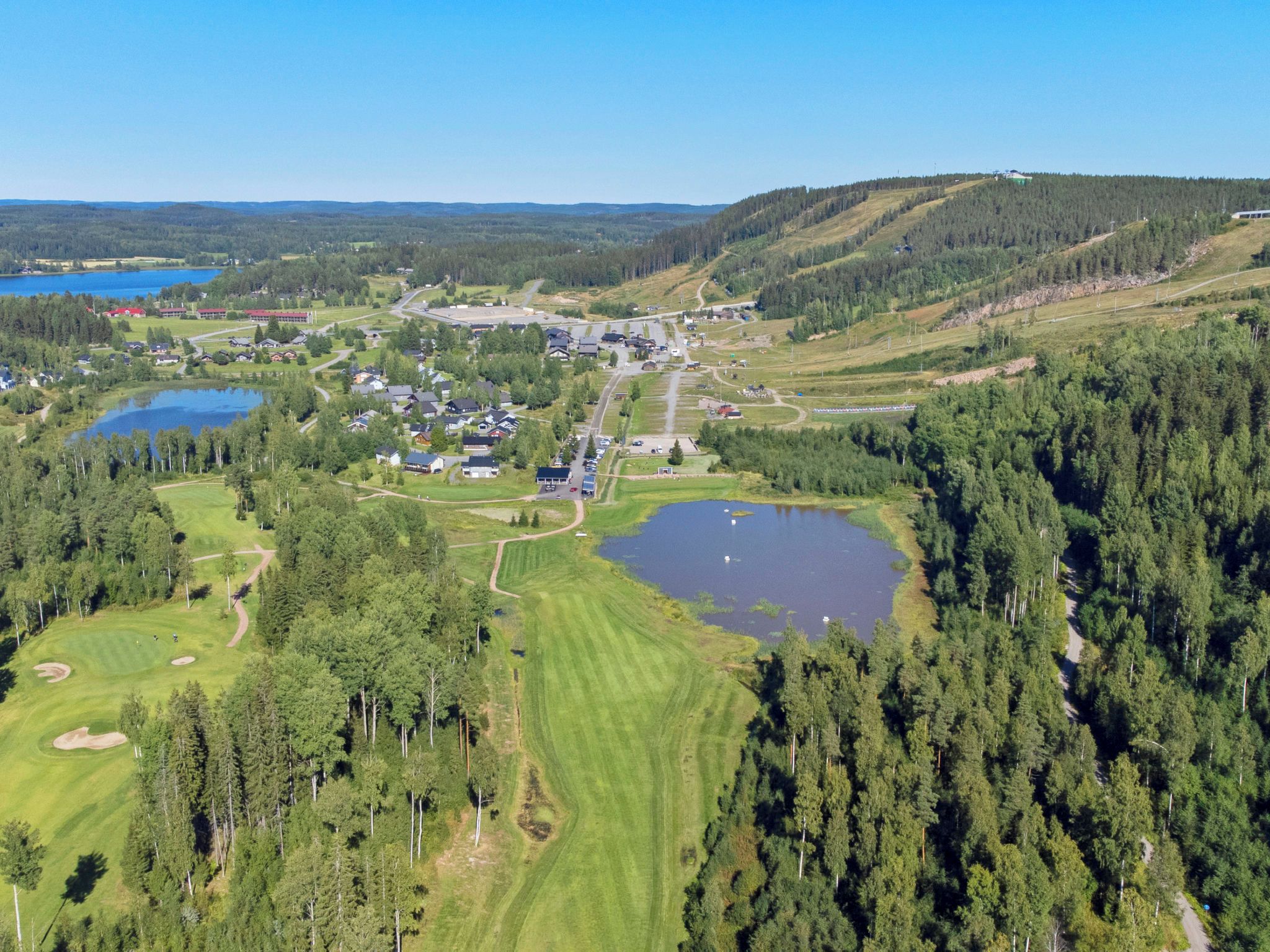 An aerial view of a golf course with multiple ponds, surrounded by dense forests and a small town with buildings and roads.