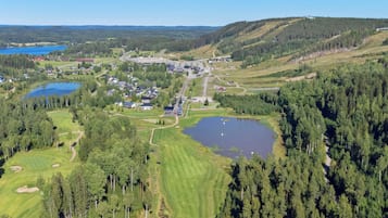 An aerial view of a golf course with multiple ponds, surrounded by dense forests and a small town with buildings and roads.