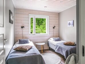 Ein Zimmer mit zwei Betten, einem kleinen Tisch, einem Fenster mit Blick auf Grünflächen und einem Wandbild.