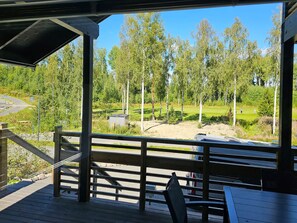 A covered outdoor area with a wooden deck, a metal railing, and a view of a golf course. - Himoksen keiju 1 by Interhome (Kuhmoinen)