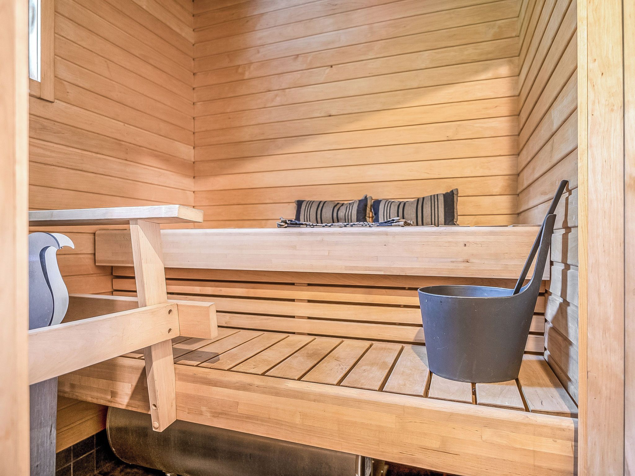 A sauna room with wooden benches, a bench seat, and a metal bucket.