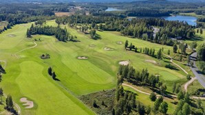 Vista aérea de un campo de golf con múltiples zonas verdes, bunkers de arena y un lago al fondo.