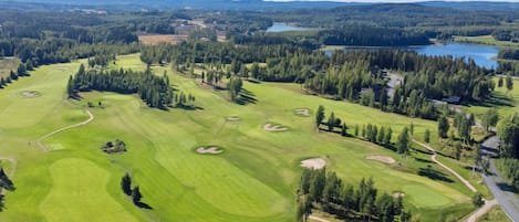 Luchtbeeld van een golfbaan met verschillende fairways, zandbunkers en een meer op de achtergrond.