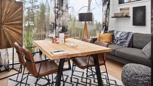 A modern living room with a wooden dining table, leather chairs, a grey sofa, and a large window offering a forest view. - Levi secret igloo revontuli 10d by Interhome (Kittilä)
