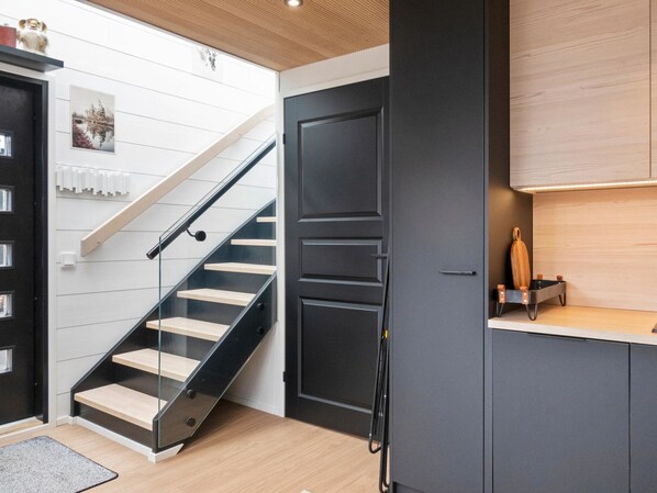A modern kitchen with a wooden countertop, a black door, and a staircase with glass railings.