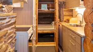 Een knus interieur van een blokhut met een bed, kitchenette en een klein raam.
