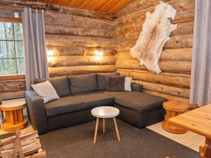 Interior de una cabaña de troncos con un sofá seccional, una mesa de centro redonda y una mesa de comedor de madera.