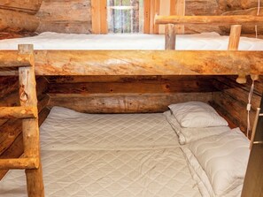 Interior de una cabaña de madera con dos literas y una cama individual.