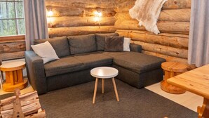 Een knus blokhutinterieur met een hoekbank, een ronde houten tafel en een opbergwand met een bontvliesdecoratie.