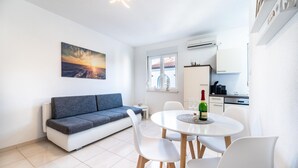 A modern living room with a grey sofa, a dining table with chairs, and a kitchen area with cabinets and an air conditioning unit. - Cozy apartment in Biograd na Moru with WiFi (Biograd na Moru)