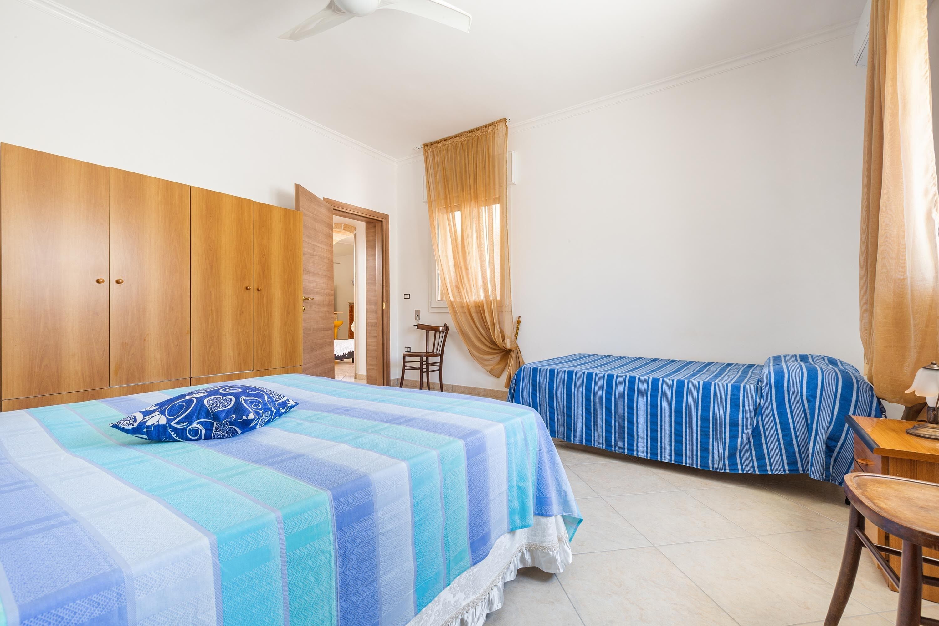 A bedroom with a large bed, a smaller bed, a wooden wardrobe, a desk, and a chair.