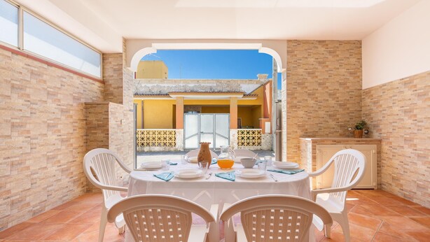 A dining area with a table set for four, white chairs, and a view of a building through an archway. - 2907 Casa la Terrazza by Barbarhouse (Manduria)