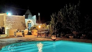 Une piscine illuminée la nuit, avec un bâtiment en pierre et un kiosque en arrière-plan.