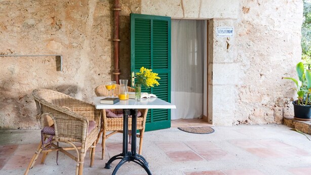 A rustic outdoor seating area with wicker furniture and a table, a green shutter door, and a potted plant. - Apartment 1 bedroom (Sineu)