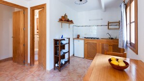 A compact kitchen with a wooden table, a bowl of fruit, and a small shelf with kitchenware. - Apartment 1 bedroom (Sineu)