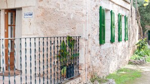 A building with a stone facade, a metal balcony with a potted plant, and green shutters on the windows. - Apartment 1 bedroom (Sineu)