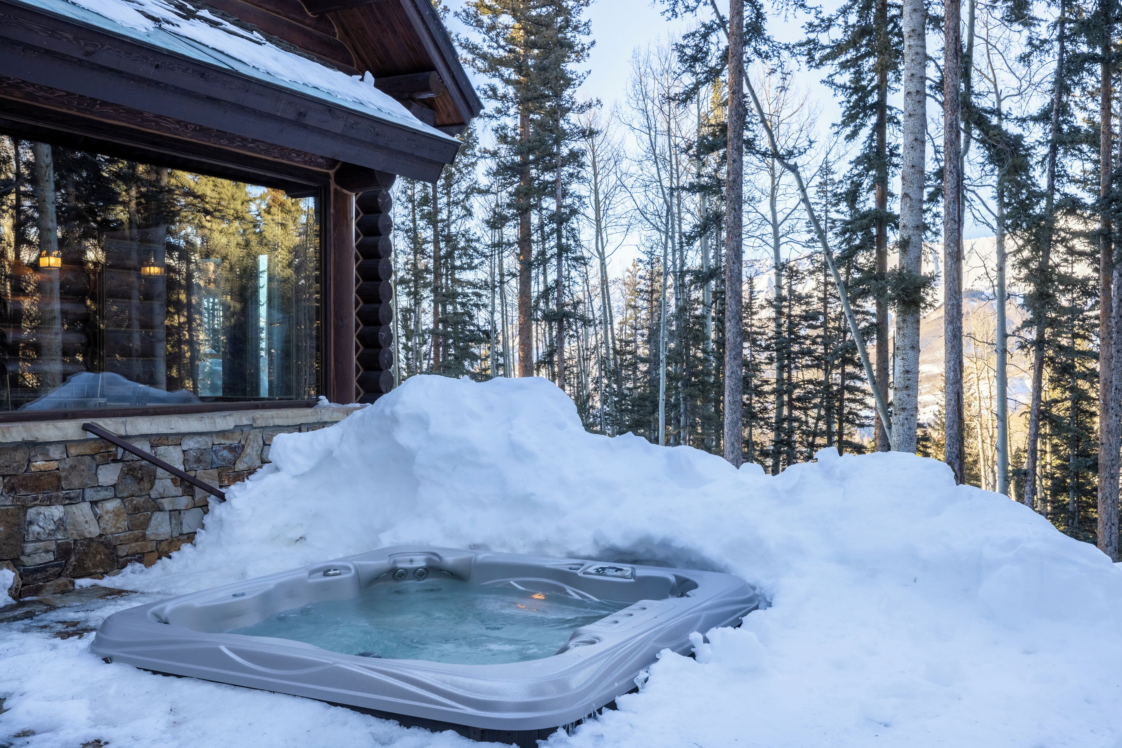 Un bain à remous entouré de neige, avec une forêt en arrière-plan.