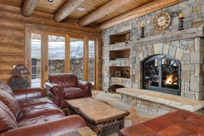 A log cabin interior with a stone fireplace, leather furniture, and a stone wall.