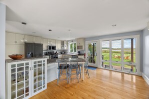 A spacious kitchen with a large island, modern appliances, and a view of a grassy landscape through large sliding doors. - A Wave from it All (Scarborough)