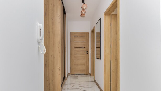 A hallway with a wooden door, a telephone, and a mirror on the wall.