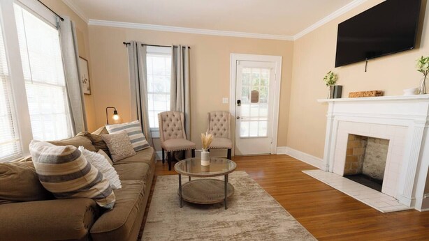 A living room with a sofa, armchairs, a coffee table, a fireplace, and a TV mounted on the wall. - Modern 2BR Cottage | Pets Allowed Near Capitol (Montgomery)