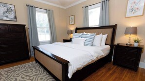 A neatly arranged bedroom with a large bed, dark wooden headboard, two bedside tables with lamps, a dresser, and a patterned rug. - Modern 2BR Cottage | Pets Allowed Near Capitol (Montgomery)