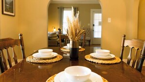 A dining table set with white plates and bowls, a vase with dried plants, and woven placemats. - Modern 2BR Cottage | Pets Allowed Near Capitol (Montgomery)