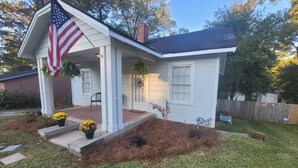 A single-story house with a porch, an American flag, and a well-maintained lawn. - Modern 2BR Cottage | Pets Allowed Near Capitol (Montgomery)