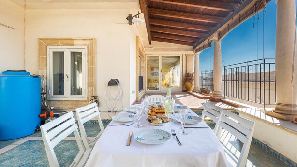 An outdoor dining area with a table set for two, white chairs, and a blue water tank in the background. - 2795 Casa Palma by Barbarhouse (Maruggio)