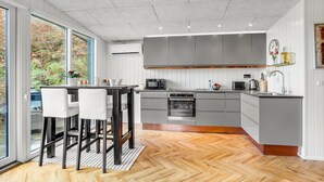 Una cocina moderna con armarios grises, suelo de madera en patrón de espiga y comedor con sillas blancas.